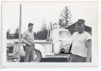 Old black and white photo of two men beside an early Reese Electric pickup truck