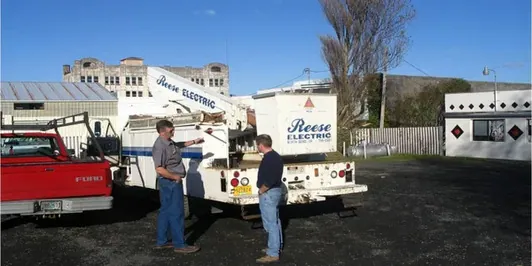 Two Reese Electric crew members talking beside a boom truck