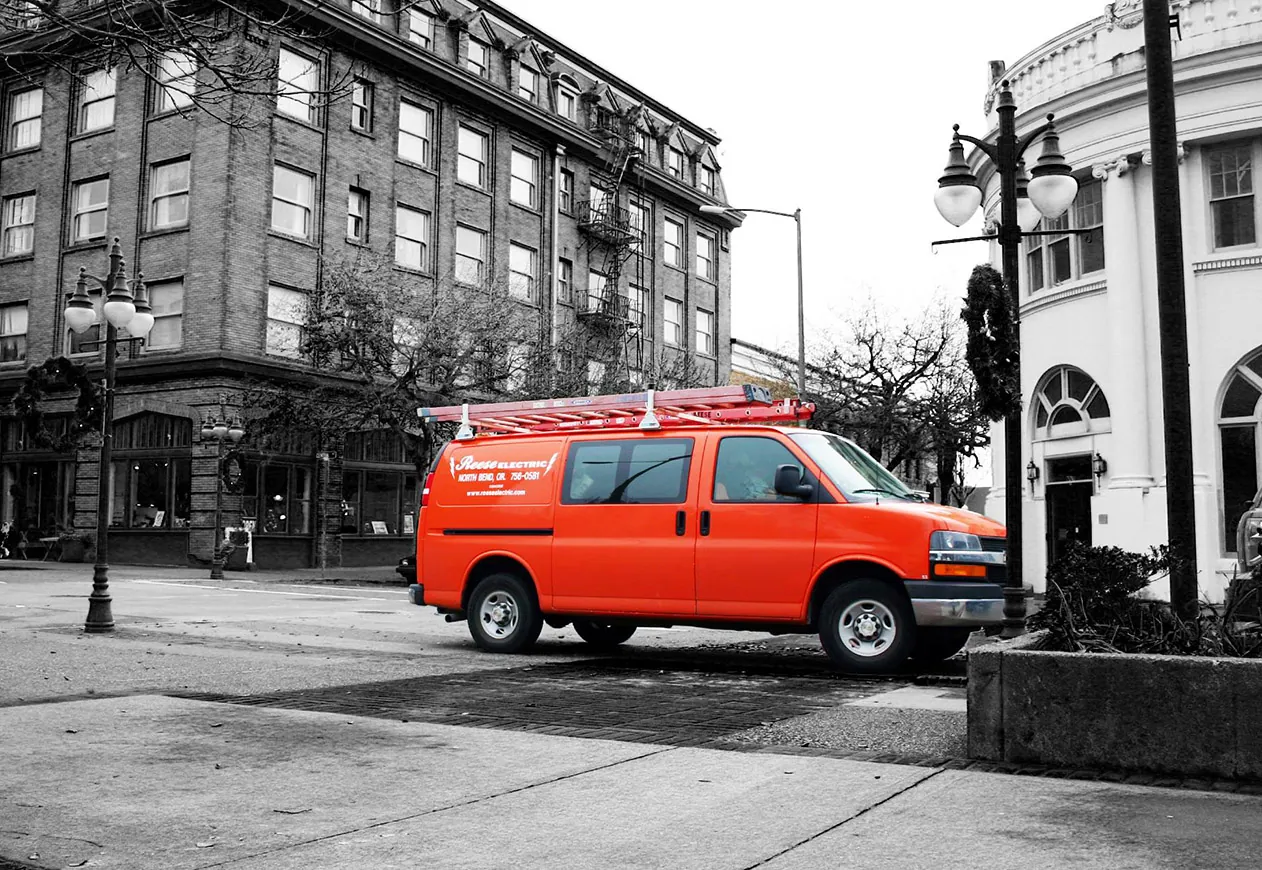 Orange Reese Electric service van with a ladder rack, parked in front of an old brick building